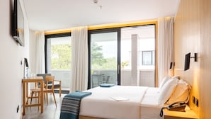 Habitación de hotel con cama, escritorio, silla y balcón con mesa y sillas.