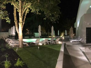 A nighttime outdoor pool area with lounge chairs and umbrellas.