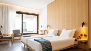 Una habitación de hotel con dos camas, un escritorio, una silla y un ventanal grande.