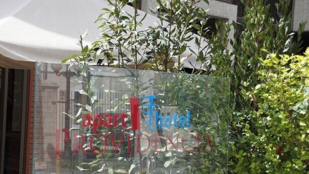 A glass window with the text "apart Hotel PROVINCIA Roman Diaz 496" and surrounding greenery.
