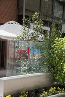 Un ventanal de vidrio con el texto "apart Hotel PROVINCIA Roman Diaz 496" y follaje verde circundante.