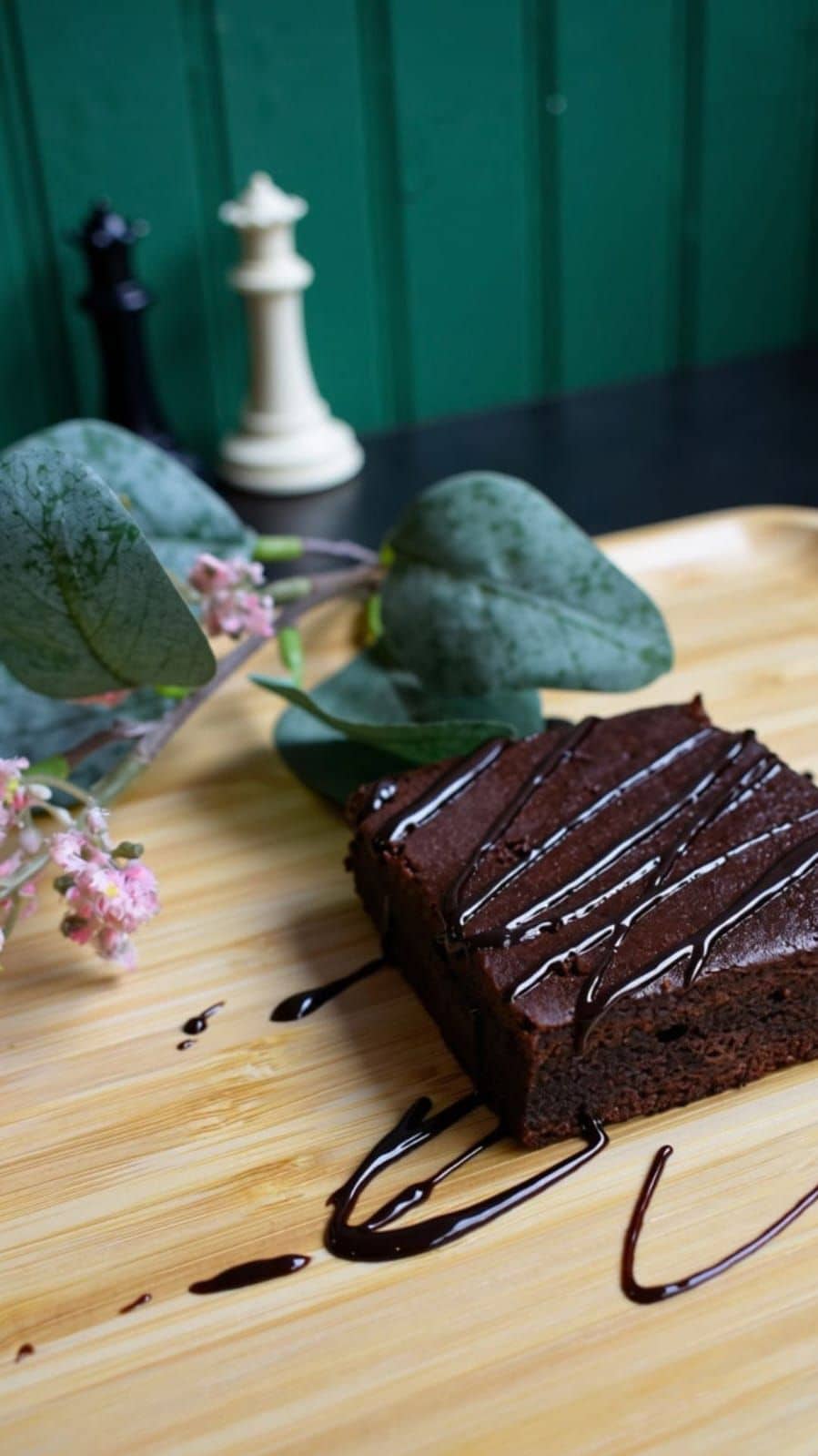 A slice of chocolate cake with chocolate sauce on a wooden board.