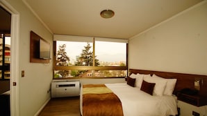 A hotel room with a large bed, a window with a city view, a mounted TV, and a small desk with a phone.
