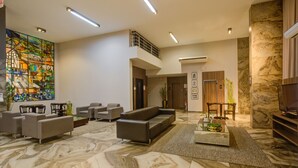 A spacious lobby with a high ceiling, a large abstract mural, a seating area with sofas and chairs, and a marble floor. - SLAVIERO Blumenau (Blumenau)