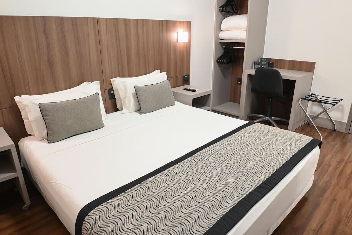 Una habitación de hotel con cama, mesitas de noche, escritorio, silla, armario y zona de baño.