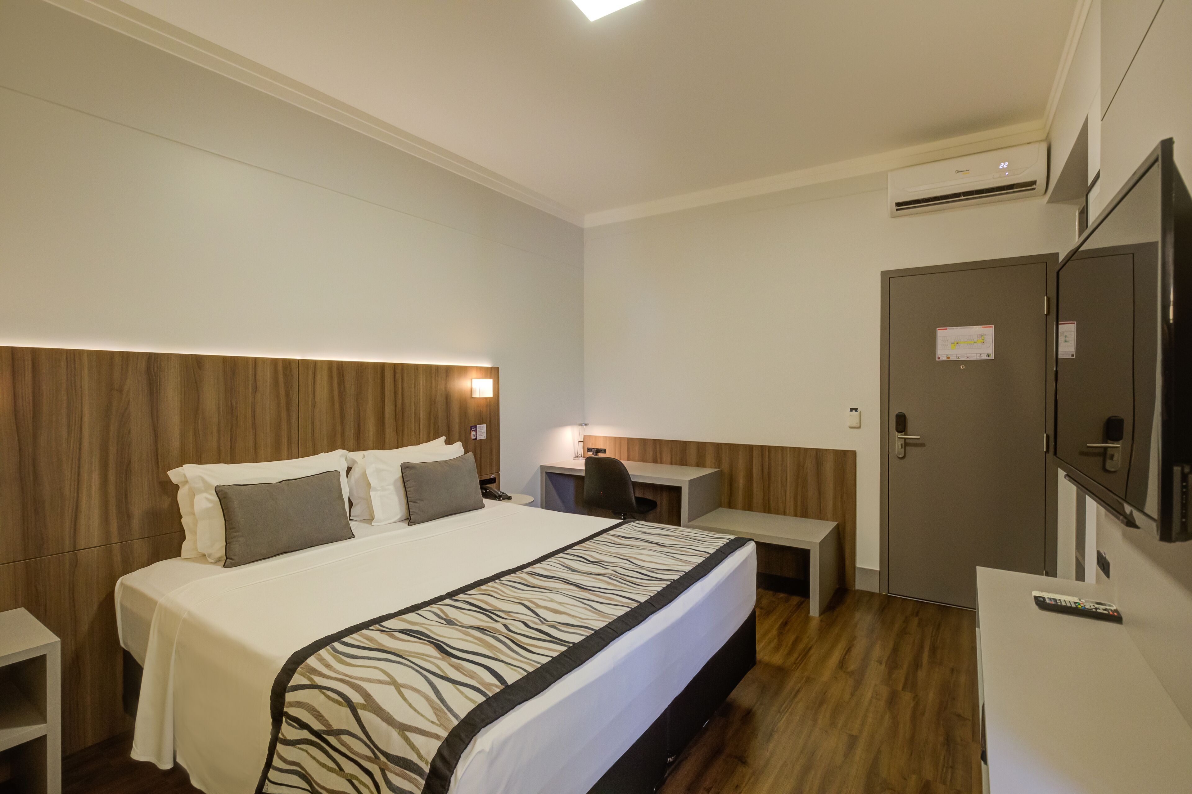 Habitación de hotel con cama, escritorio, silla, televisión y armario.