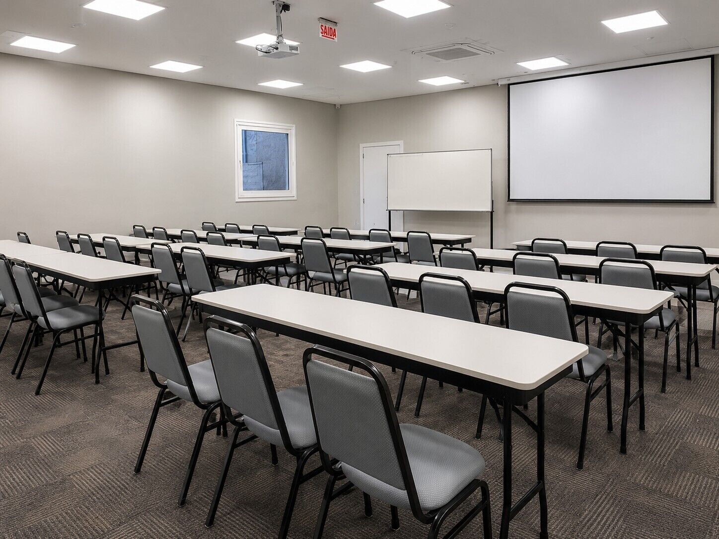 A conference room with multiple tables and chairs, a projector screen, and a whiteboard.