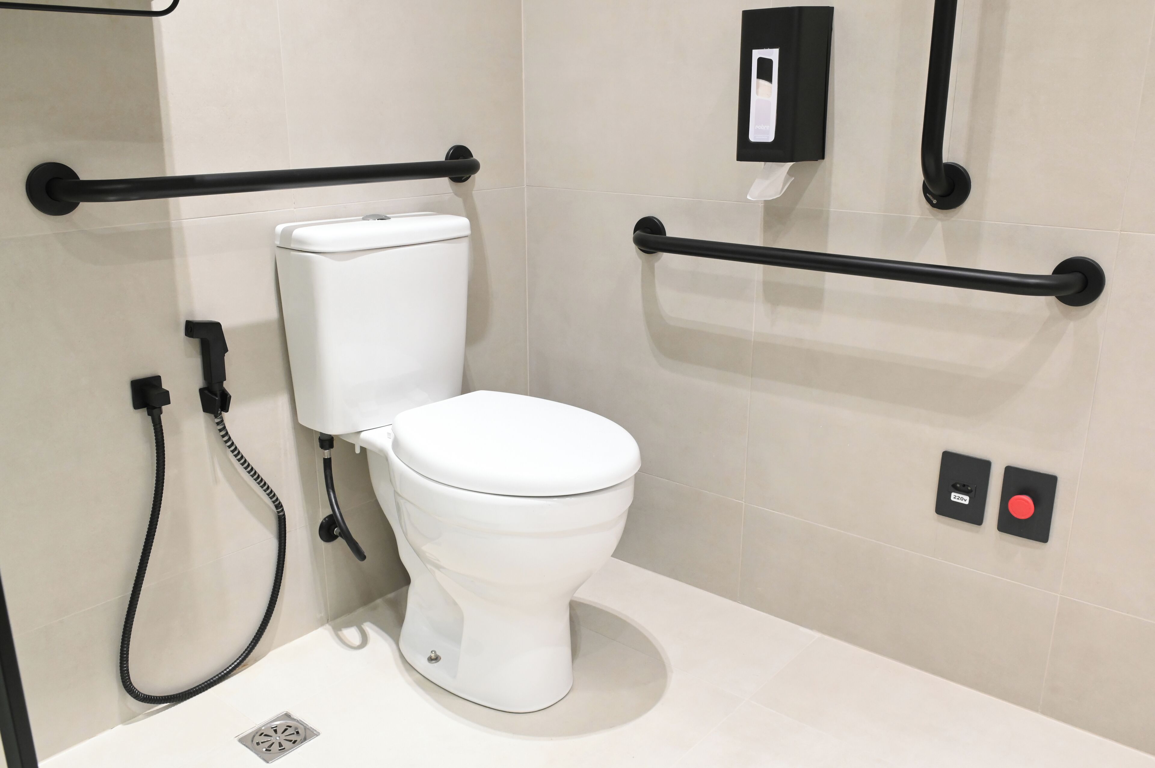 Ein modernes Badezimmer mit Toilette, Haltegriffen, einer Handbrause und einem Toilettenpapierhalter.
