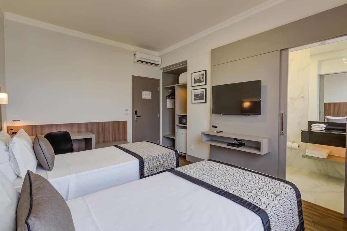 Habitación de hotel con dos camas, un escritorio, un televisor, un armario y baño.
