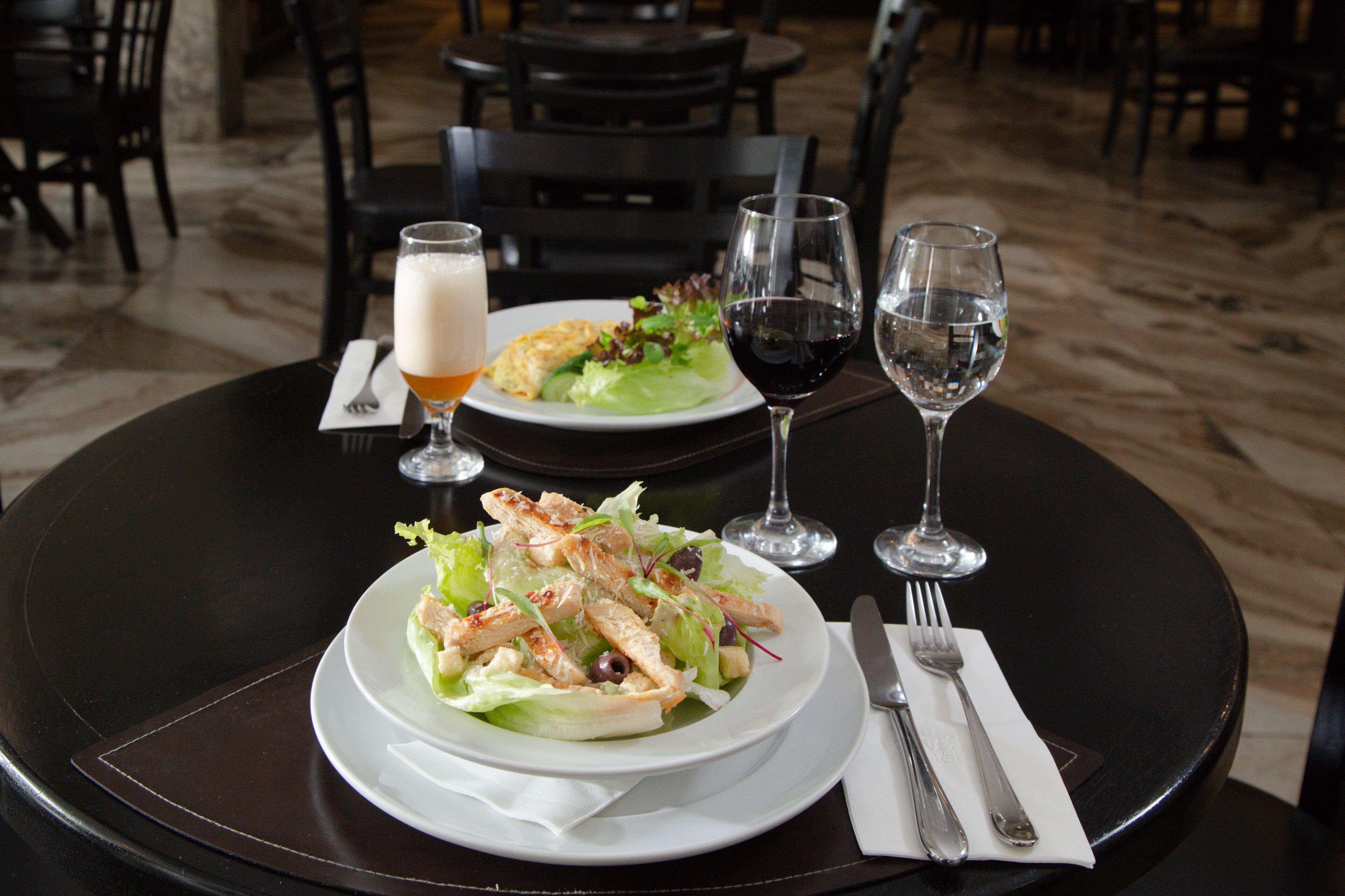 Una mesa de comedor con una ensalada, dos copas de vino y una cerveza.
