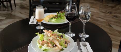 Una mesa de comedor con una ensalada, dos copas de vino y una cerveza.