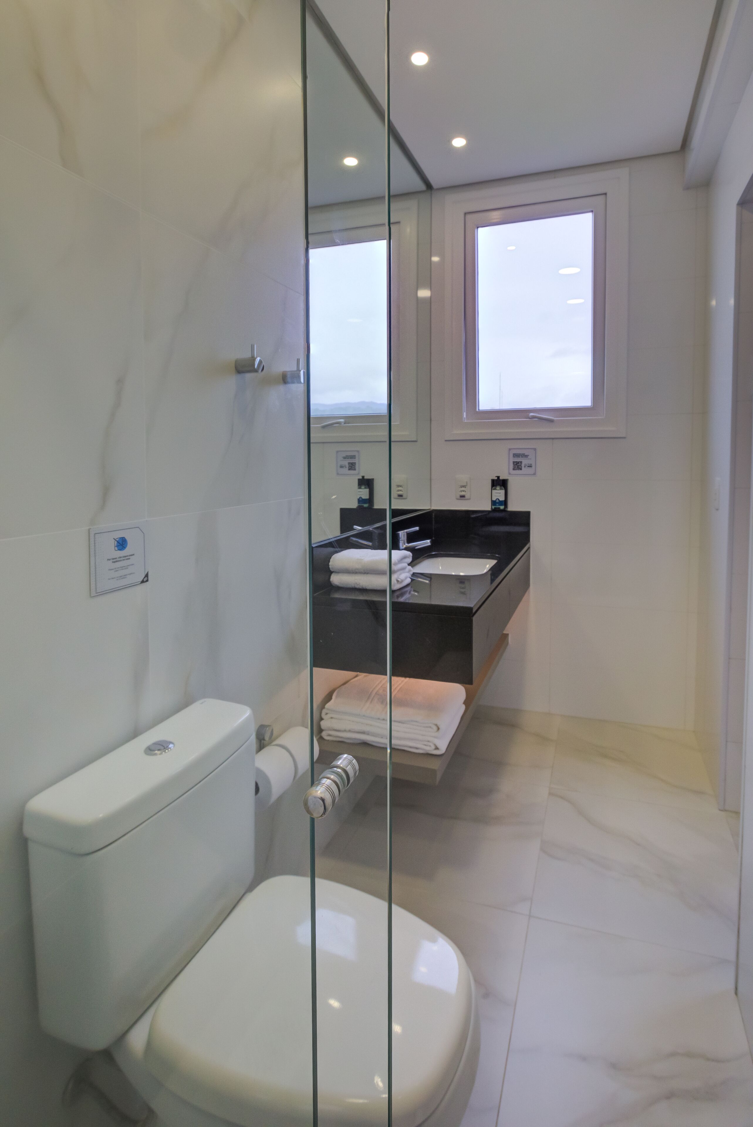 Un baño moderno con mampara de vidrio, inodoro, lavabo y espejo.
