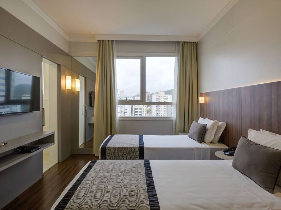 Quarto de hotel com duas camas, televisão, escrivaninha e janela com cortinas.