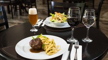 Una mesa con un plato de pasta y carne, dos copas de vino y una jarra de cerveza.