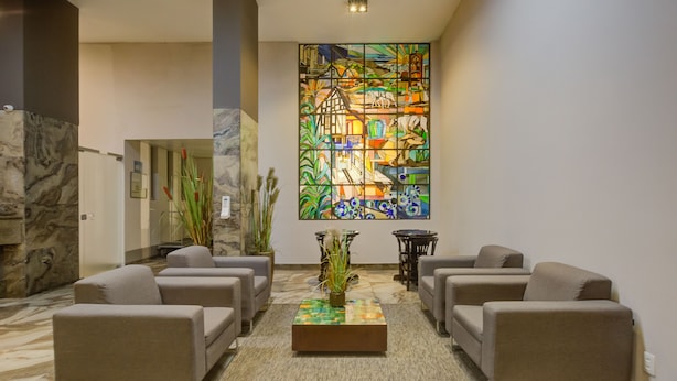 A lobby with a large stained glass window, a marble floor, and a seating area with sofas and a coffee table. - SLAVIERO Blumenau (Blumenau)