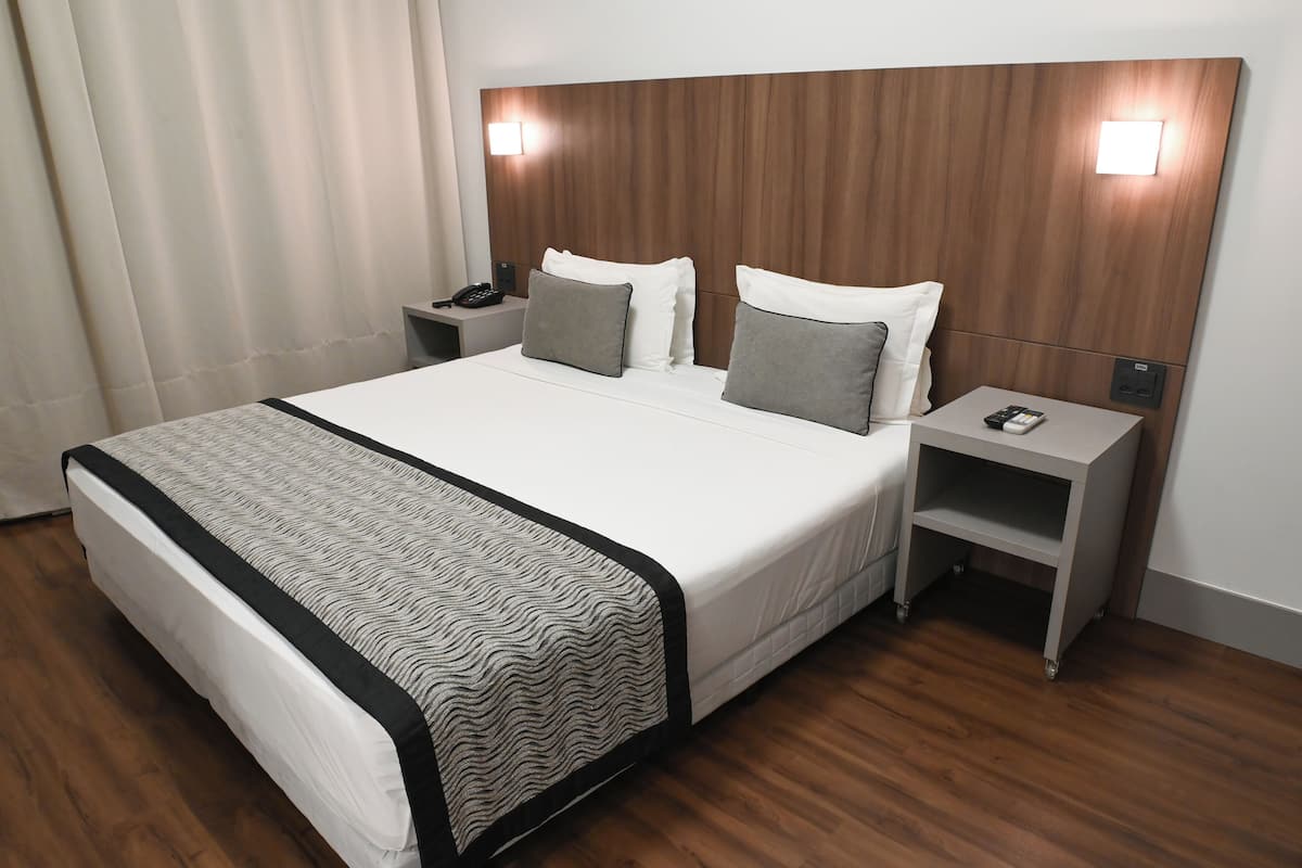 Una habitación de hotel con una cama grande, dos mesitas de noche, un teléfono y una lámpara.