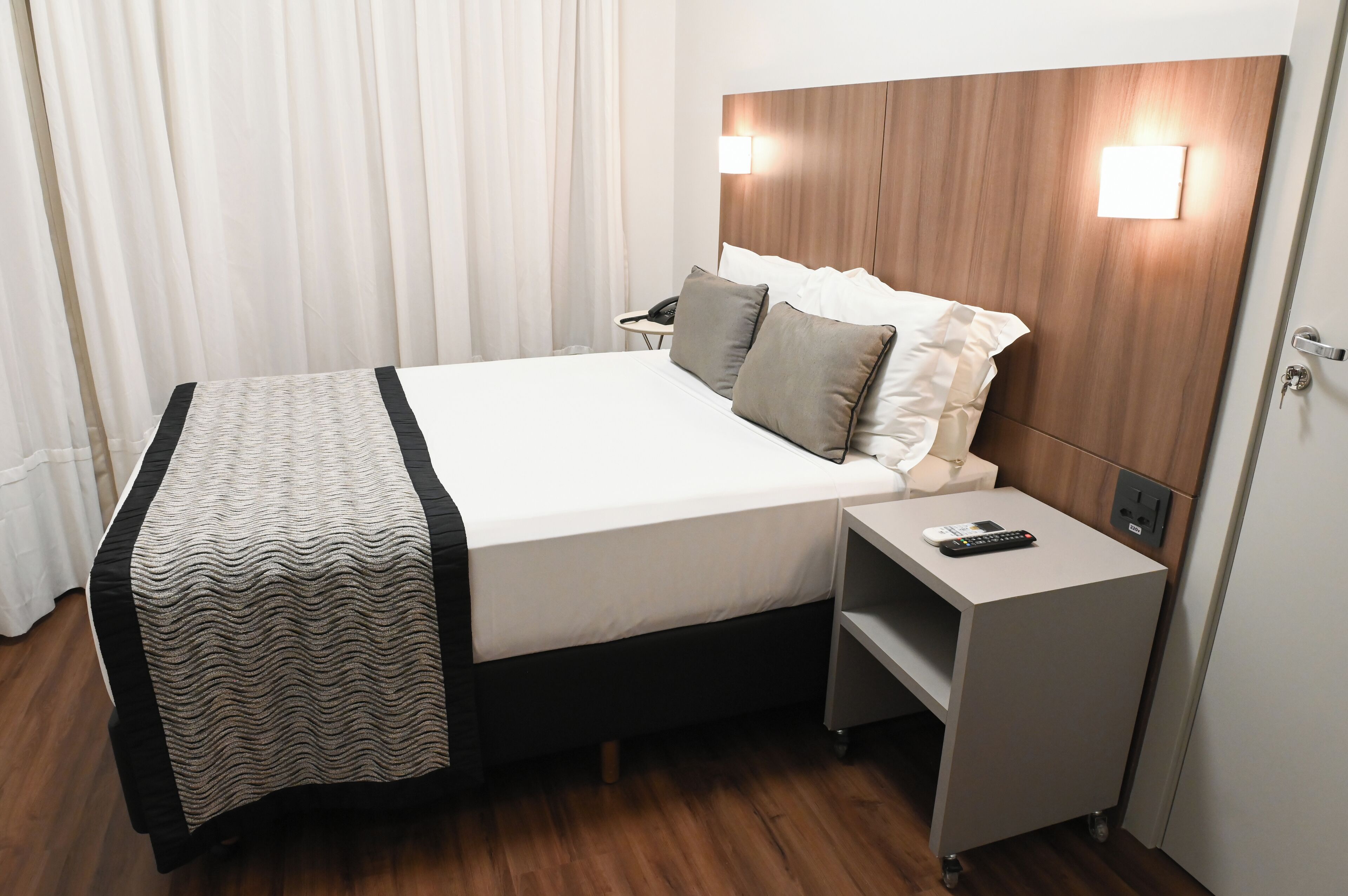 Una habitación de hotel con cama, mesita de noche y velador.