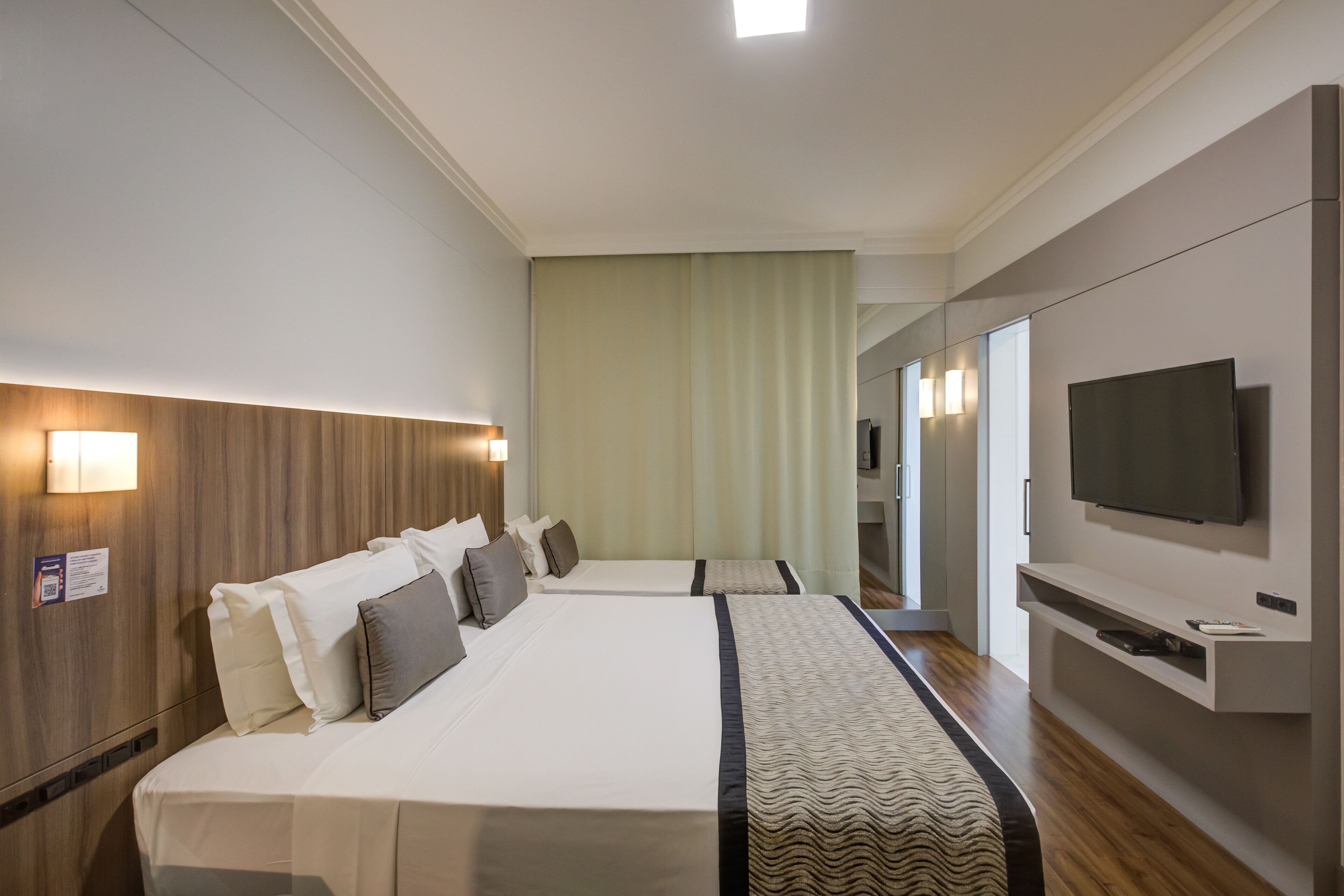 Habitación de hotel con dos camas, un televisor y un ventanal con cortinas.