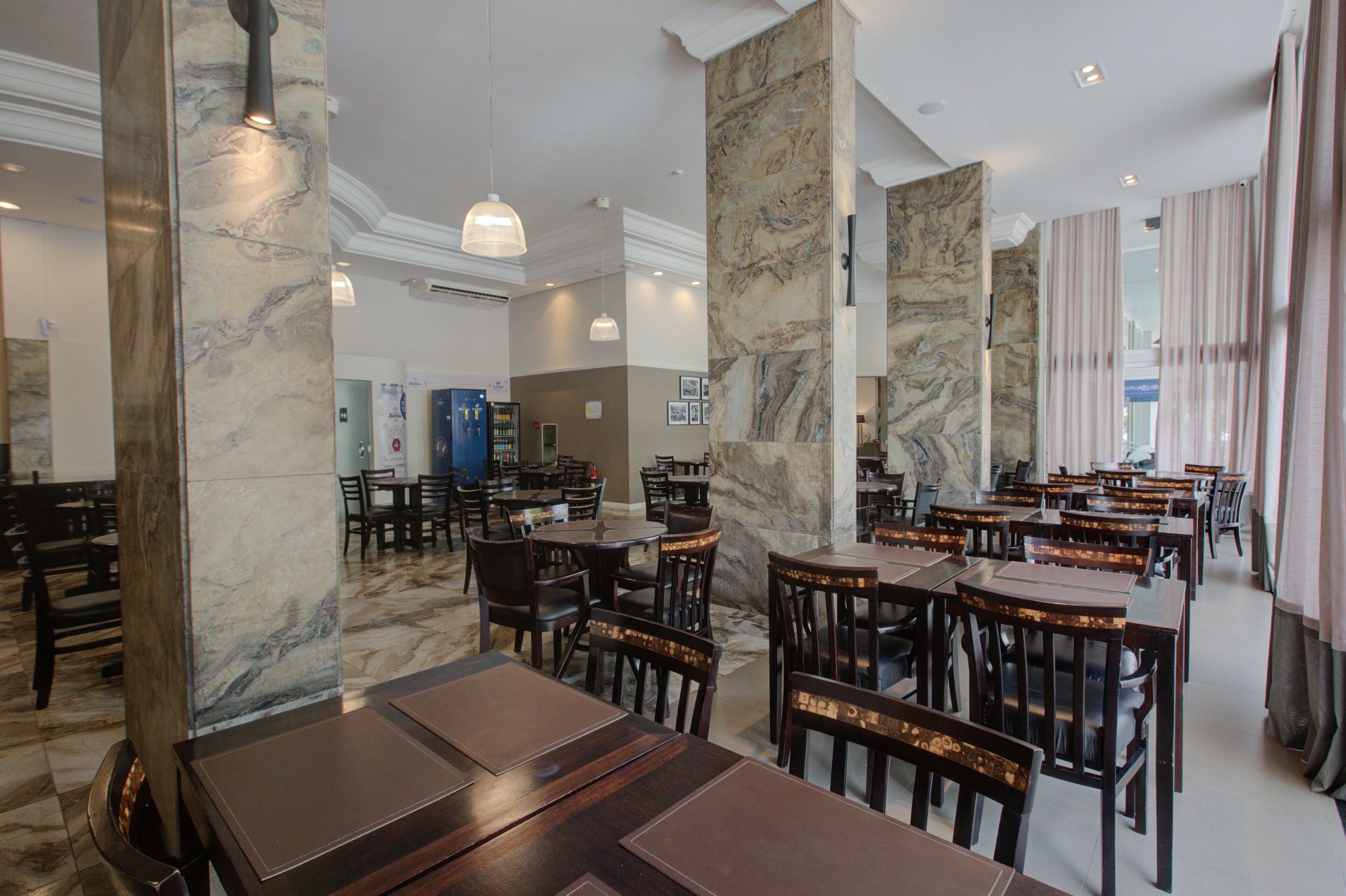 A spacious restaurant with marble columns, wooden tables, and chairs.