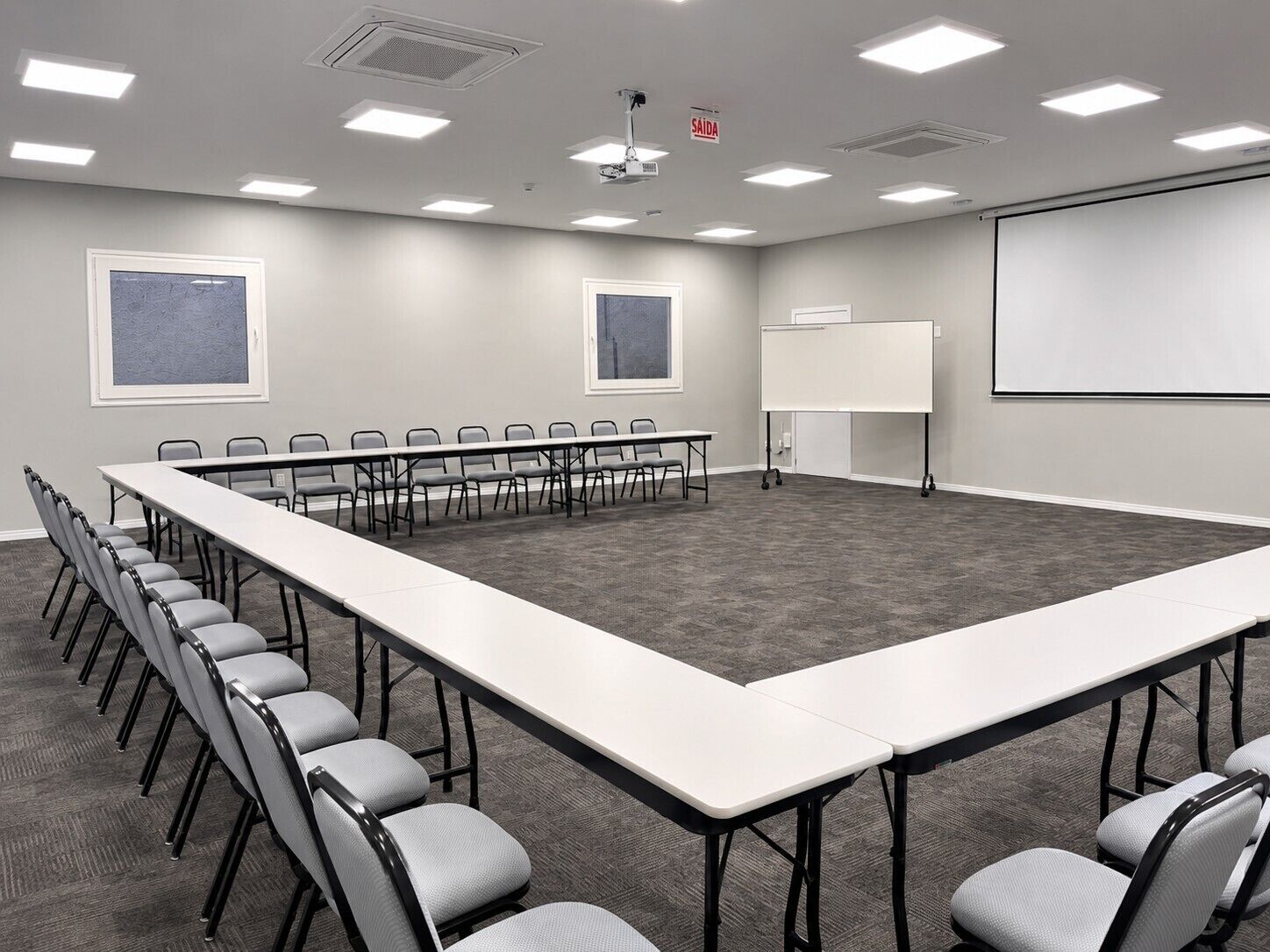 A conference room with a long table, chairs, a whiteboard, and a projector screen.