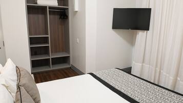 Habitación de hotel con cama, armario con estantes, televisor de pantalla plana y cortina.