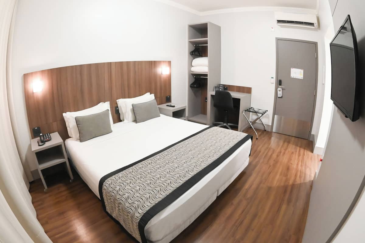 Habitación de hotel con una cama grande, un escritorio, una silla, un armario y un televisor.