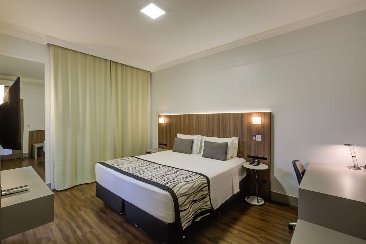 Una habitación de hotel con cama, mesita de noche y escritorio con lámpara.