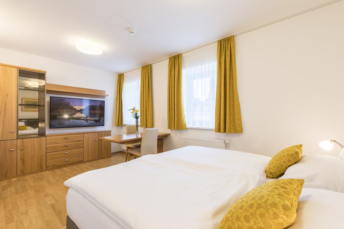 A hotel room with a bed, a desk, a television, and a window with curtains.