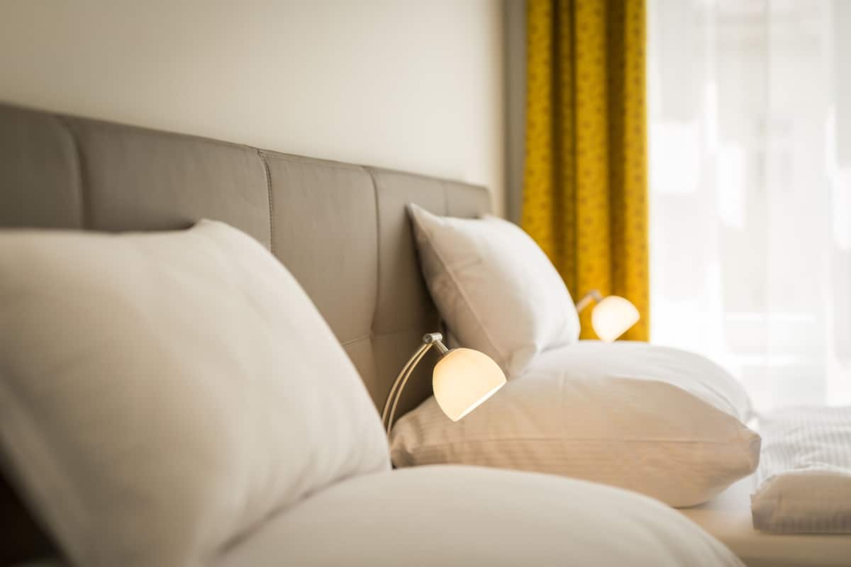 A neatly made bed with white pillows and a bedside lamp.