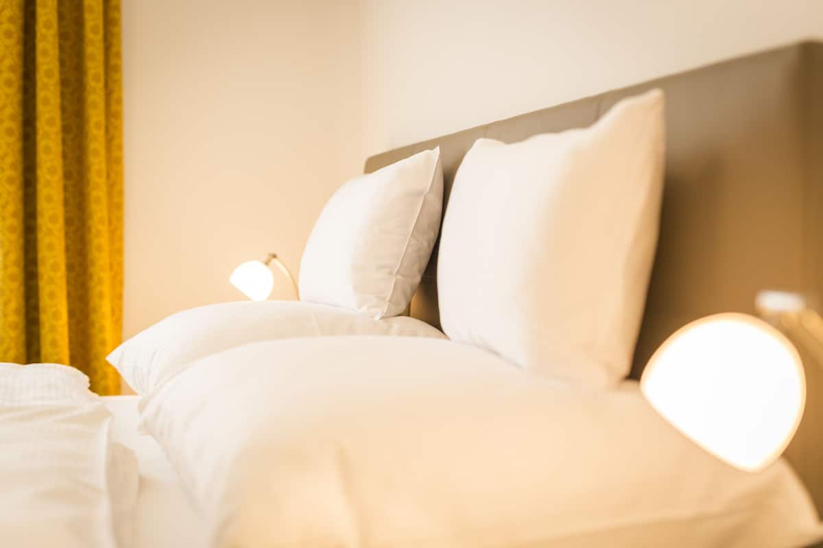 A neatly made bed with white bedding and pillows, a headboard, and a bedside lamp.