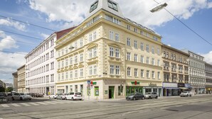 Un edificio a più piani con uno stile architettonico classico, caratterizzato da un ingresso d'angolo ben visibile e diversi locali commerciali al piano terra.