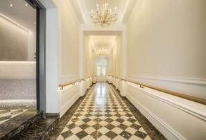 A long, elegant hallway with a checkered marble floor, white walls, and a grand chandelier. - Vienna Grand Apartments CITY (Vienna)