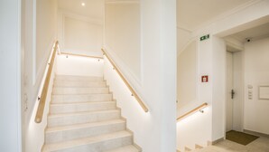 Una scala con gradini color beige e ringhiere in legno, che porta a un ascensore.
