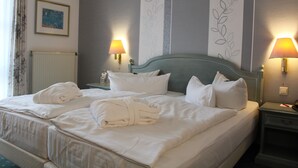 Een tweepersoonsbed met witte lakens, twee bedlampjes en een ingelijst schilderij aan de muur.