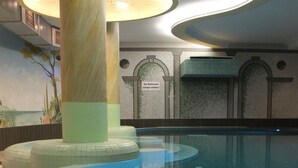 An indoor swimming pool with clear water, a tiled floor, and a modern ceiling design.