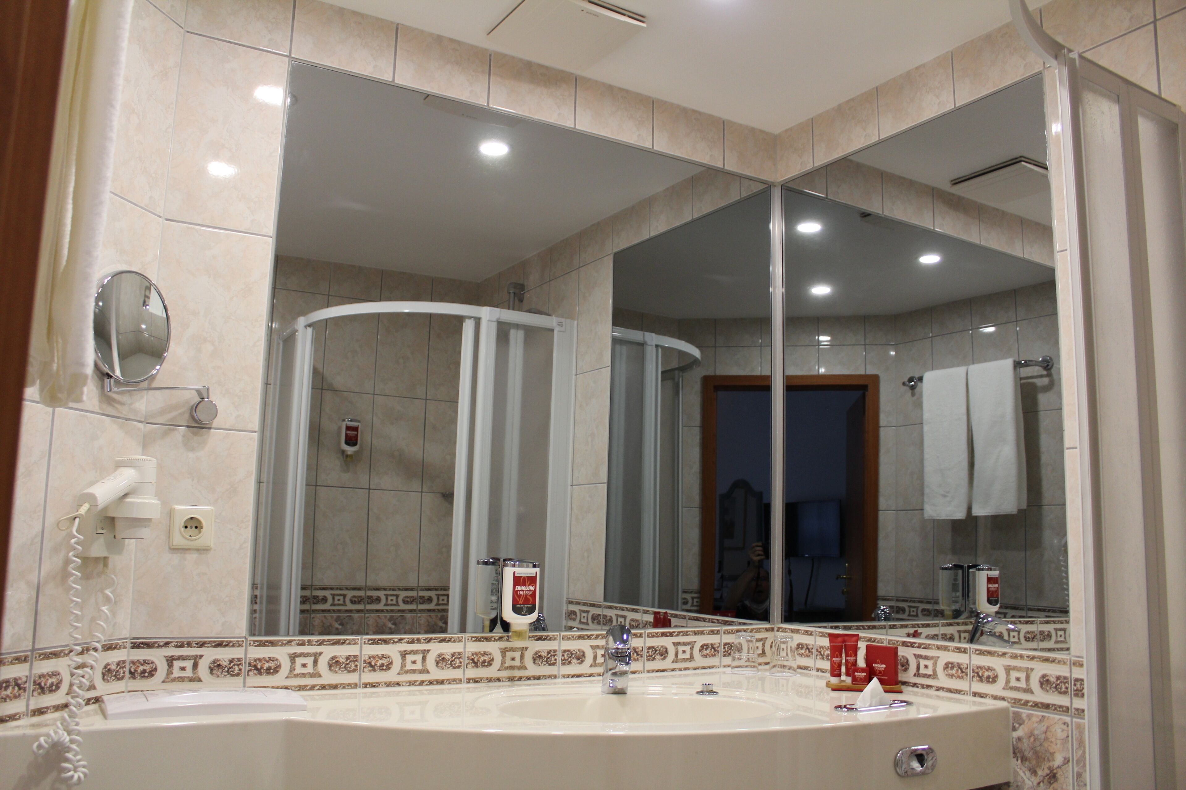 Un baño con un espejo grande, una ducha y un lavabo con toallero.