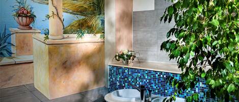 Un baño con una bañera de mosaico, una planta en maceta y un mural en la pared.