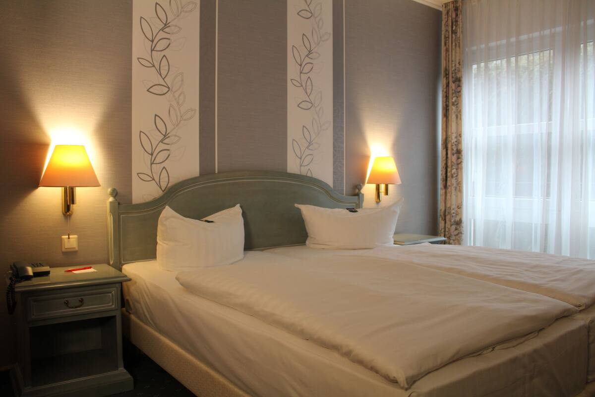 Een net opgemaakt bed met witte beddengoed en twee bedlampjes.