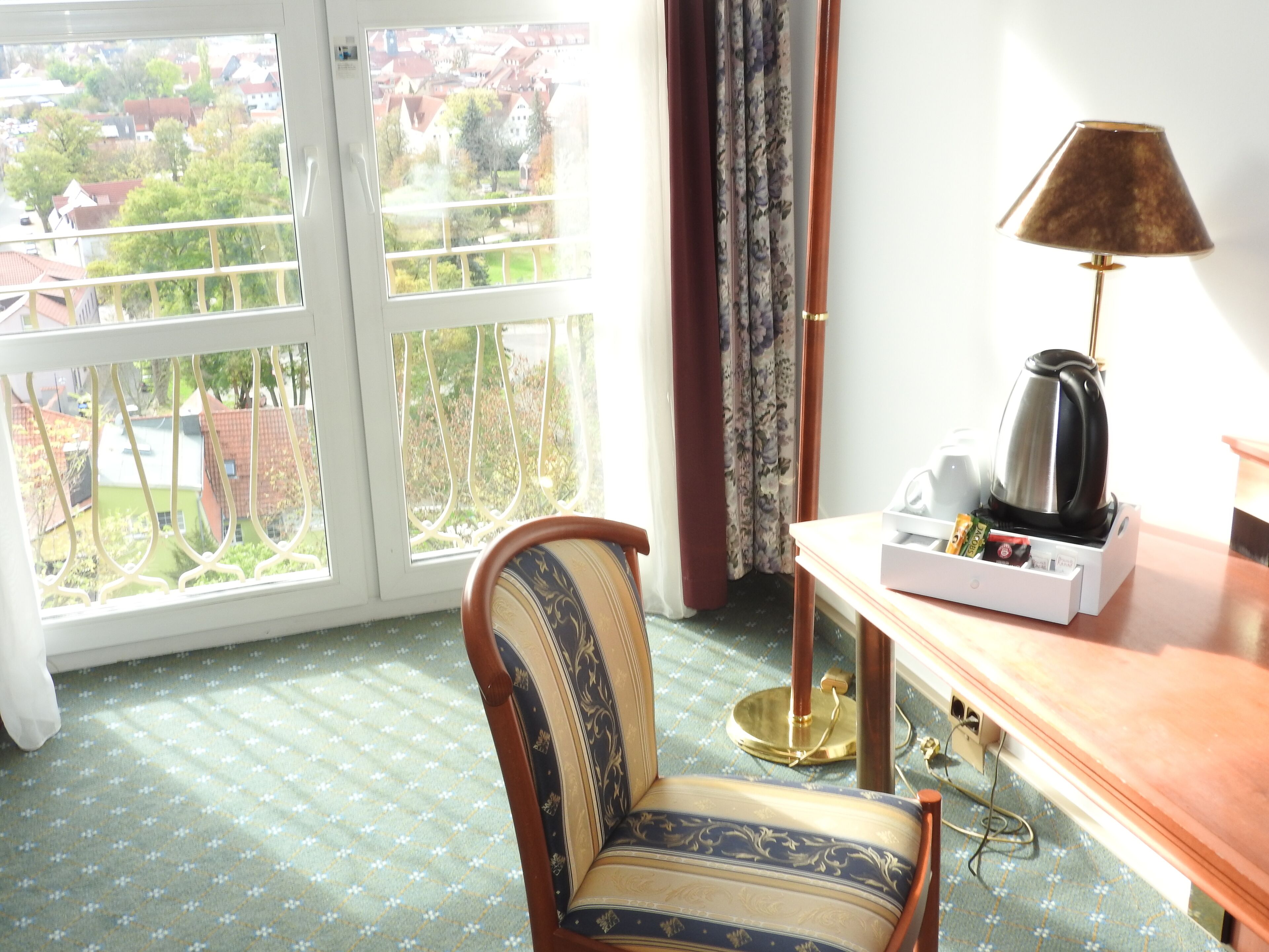 A room with a chair, a table with a lamp, a coffee maker, and a view of the outside.