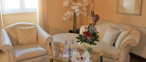 Una habitación con sofá, sillón y una mesa de centro de vidrio con botellas y flores.