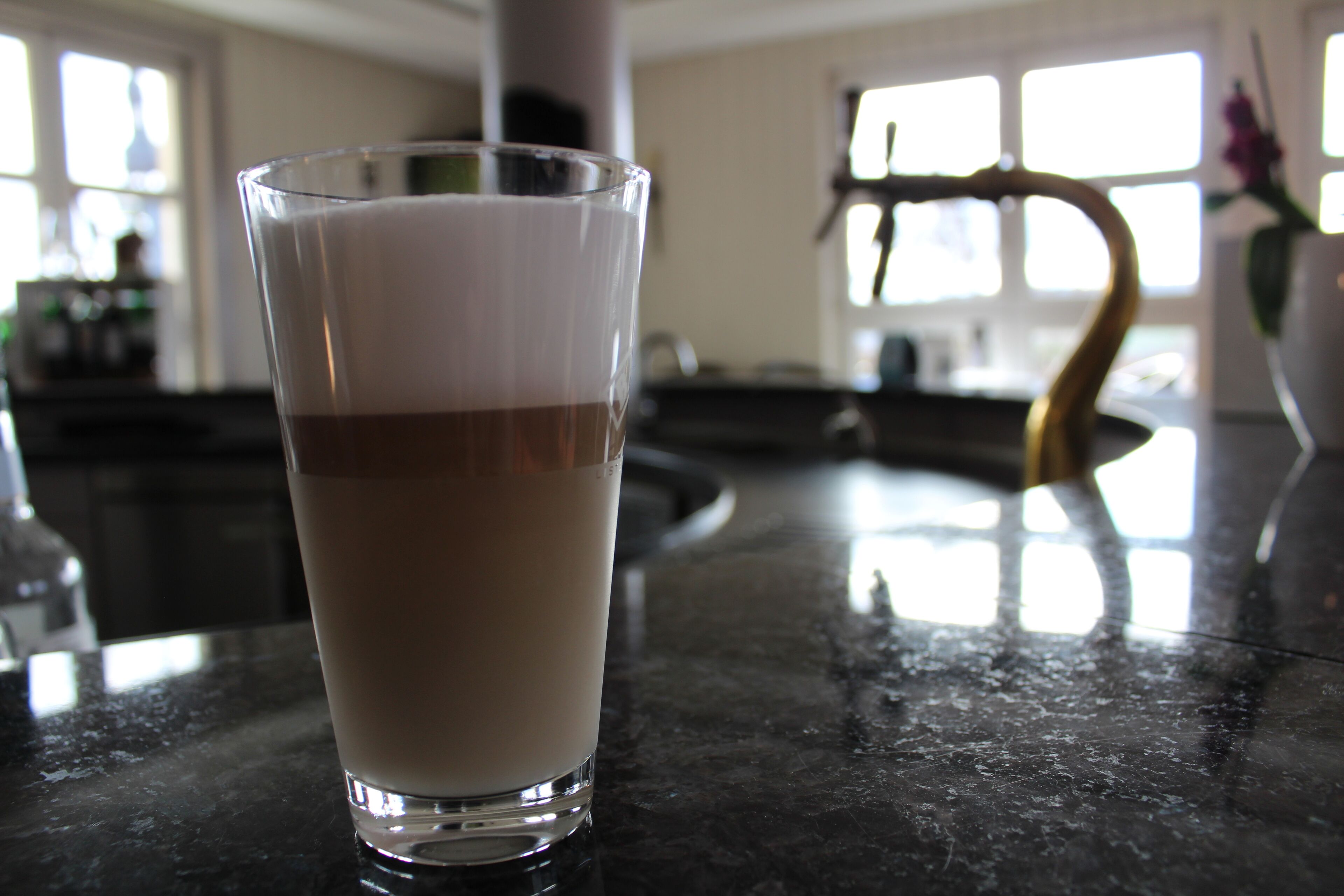 A glass of layered beverage on a reflective countertop.