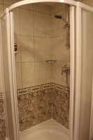 Ducha con puerta curva, paredes de azulejos y cabezal de ducha de mano.