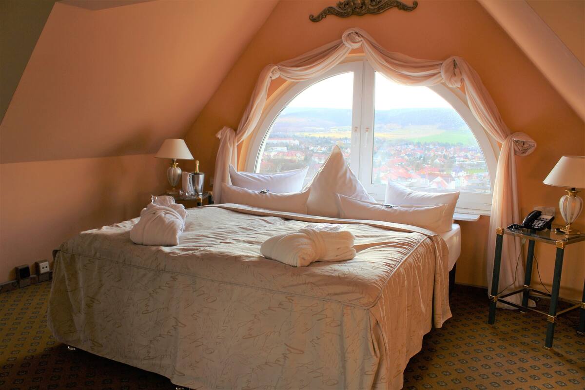 Een slaapkamer met een groot bed, twee bedlampen, een nachtkastje en uitzicht op een stad door een raam.