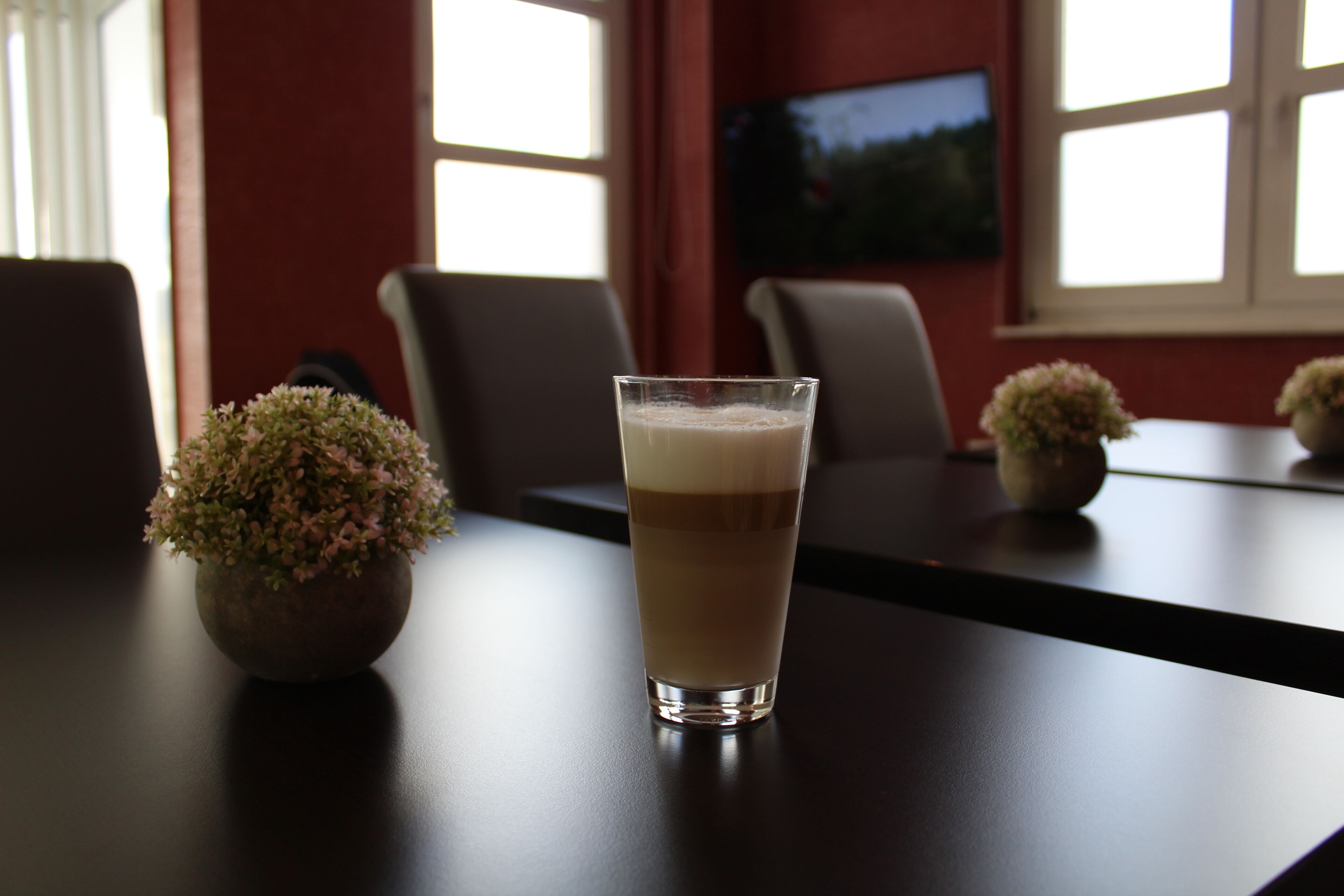 A conference table with a glass of iced coffee, a potted plant, and a television in the background.