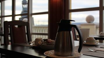 Une table sur laquelle se trouvent une cafetière, un bol de collations et une tasse, dans une pièce donnant sur un paysage grâce à de grandes fenêtres.