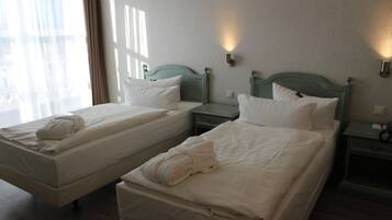Two single beds with white linens and towels, wooden headboards, and bedside tables with wall-mounted lamps.