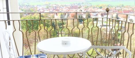 A balcony with a round table and two chairs, one with a plaid cushion.
