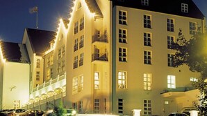 Een hotel met meerdere verdiepingen, een symmetrische gevel, diverse balkons en een rij lichtpunten langs het dak.