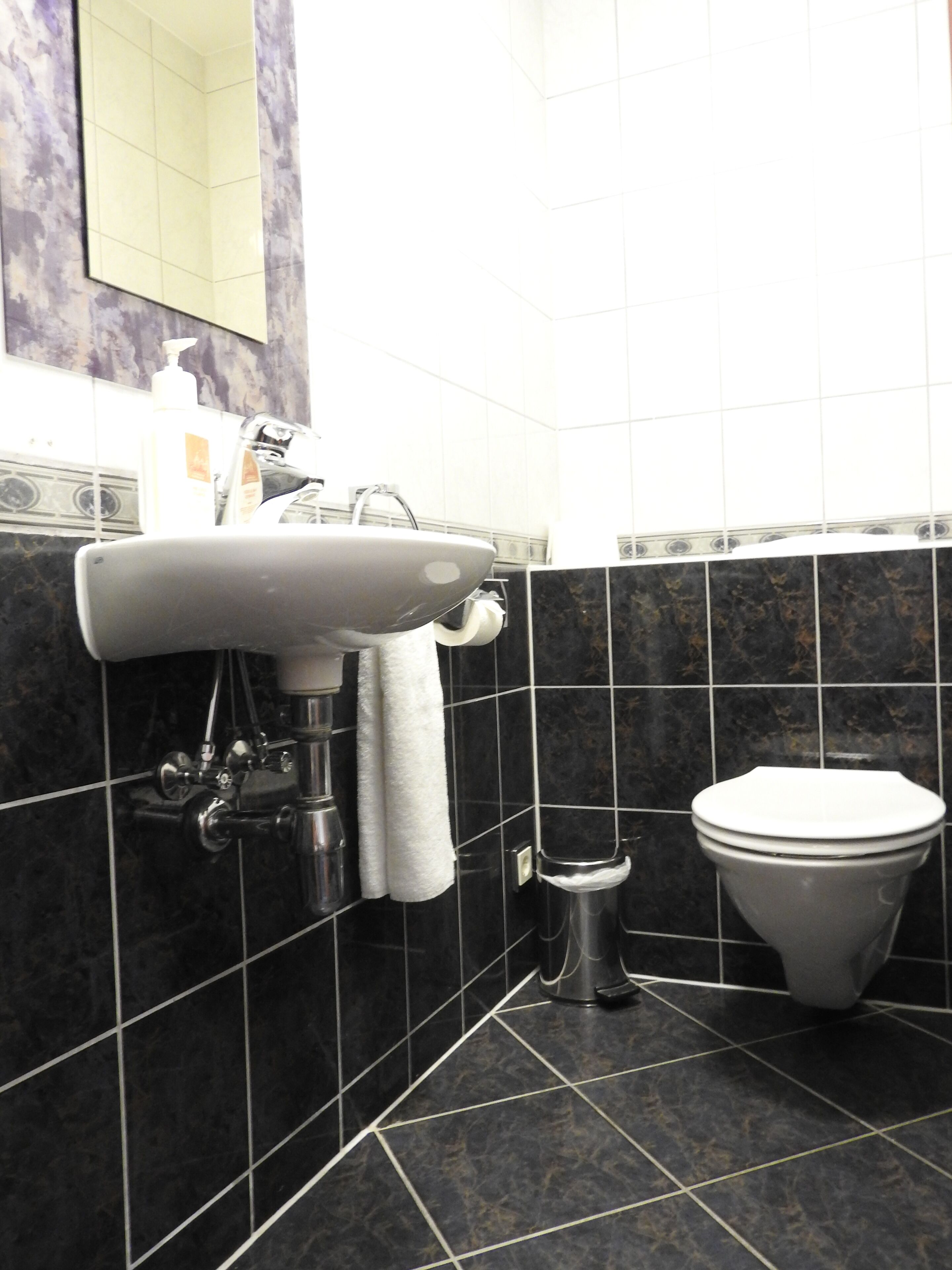 Un baño con un lavamanos blanco, un inodoro y paredes revestidas de baldosas oscuras.