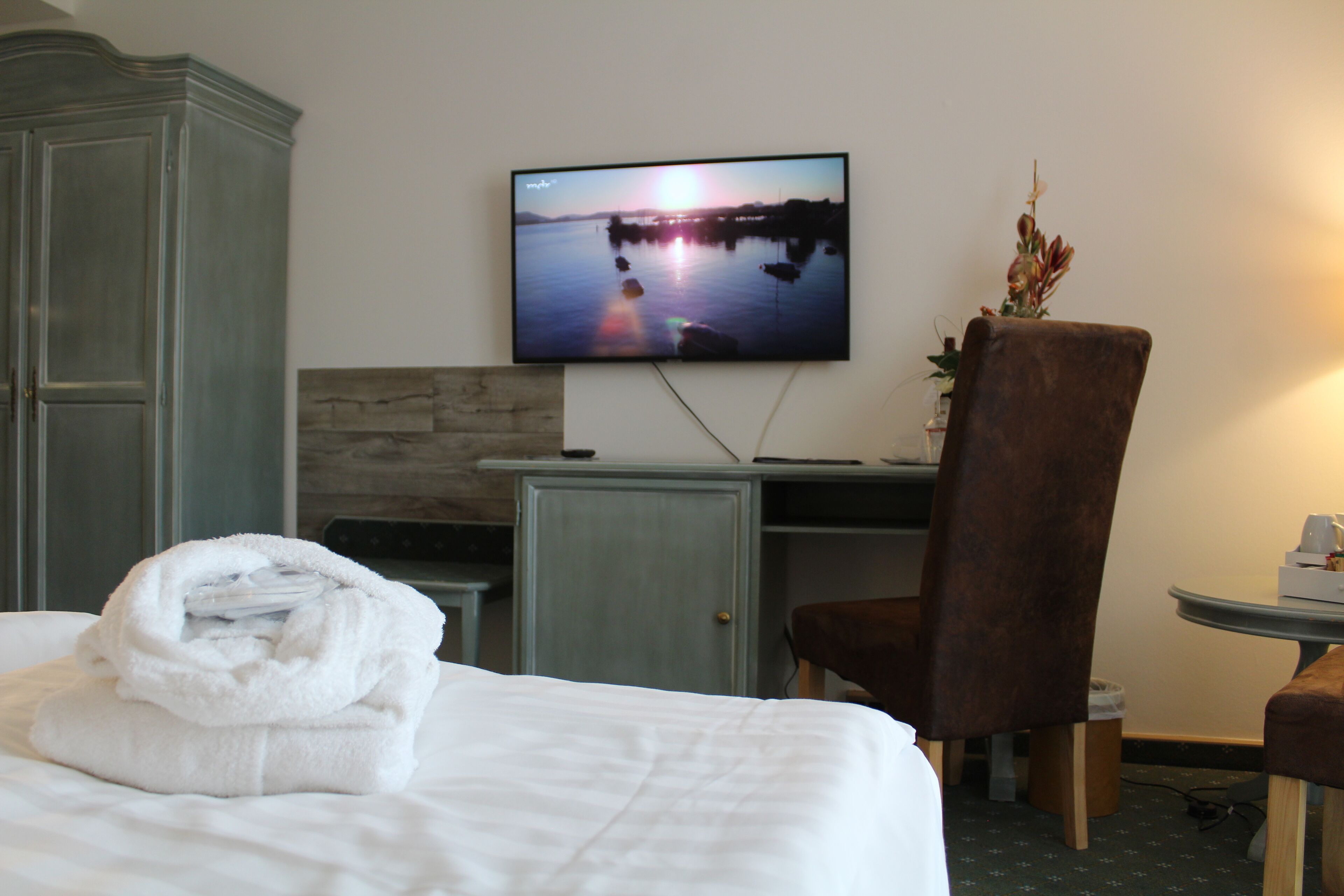 A hotel room with a bed, a TV displaying a sunset over water, a desk, and a chair.